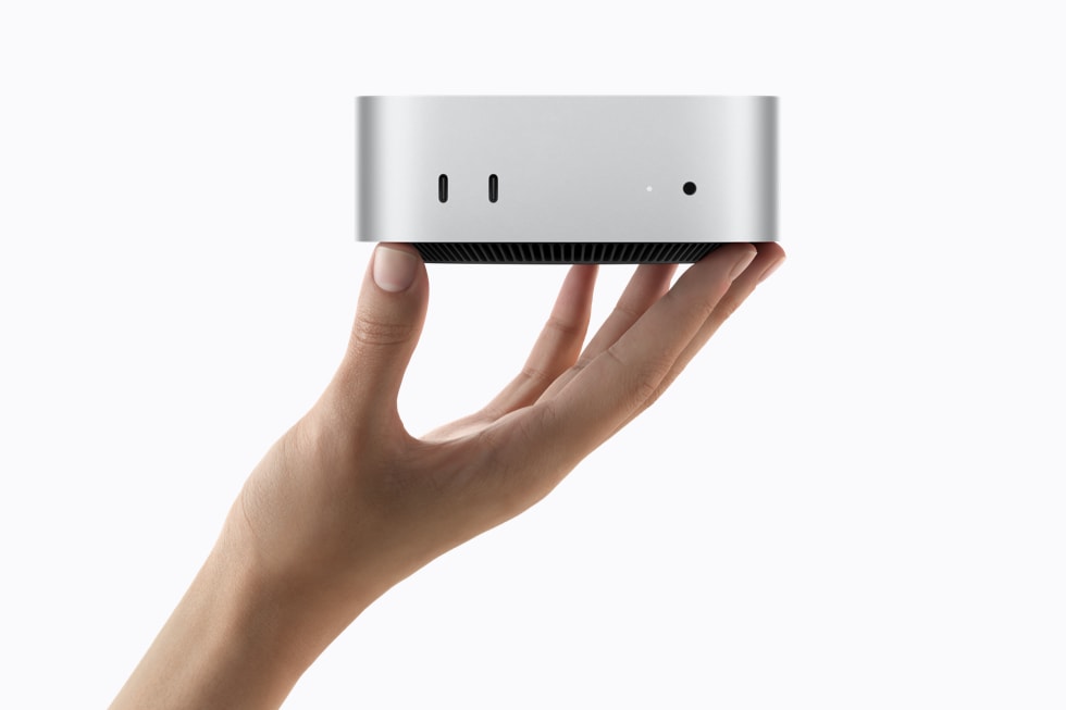 一个人手持银色 Mac mini,展示设备正面的各个端口。